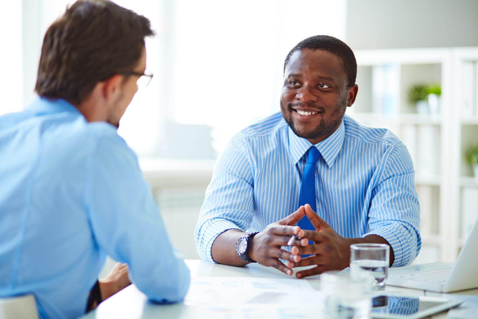 Photo of two business men in an amiable business meeting in a very bright white modern room.