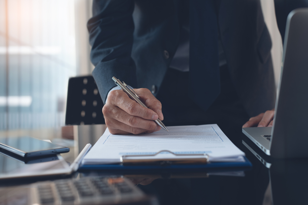 Photo of suited man's hand filling out paperwork.