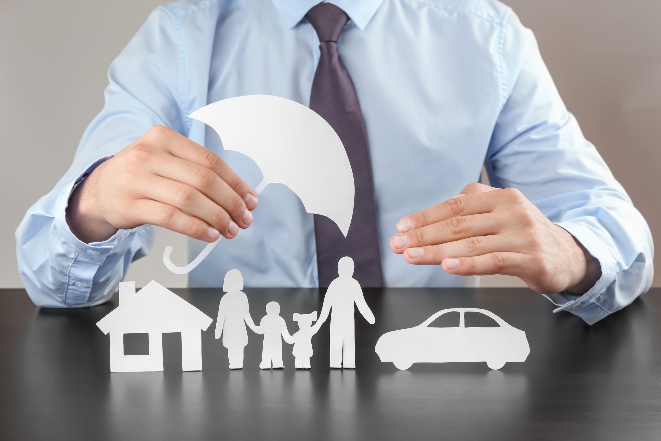 umbrella_insurance Photo of a man with a business shirt and tie holding white cutouts of an umbrella over a family of paper cutouts.
