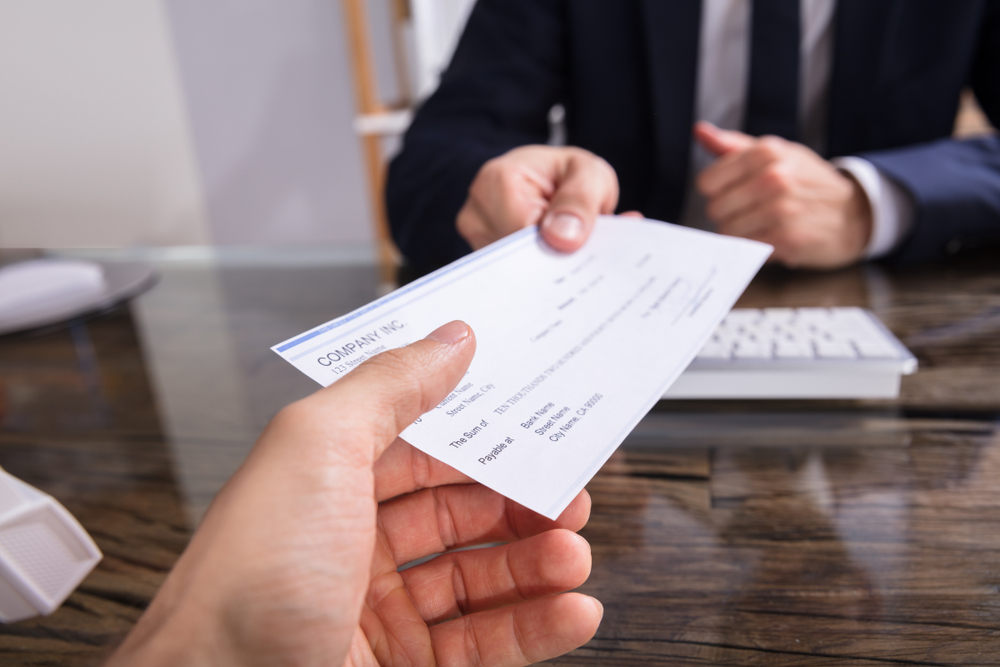 Photo of two hands over a desk clutching a passed check from one to another.